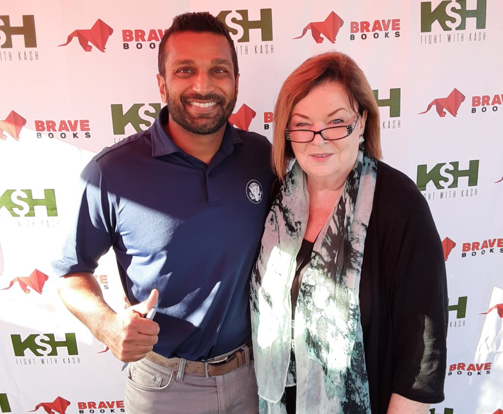Two people smiling at a photo event with logos in the background.