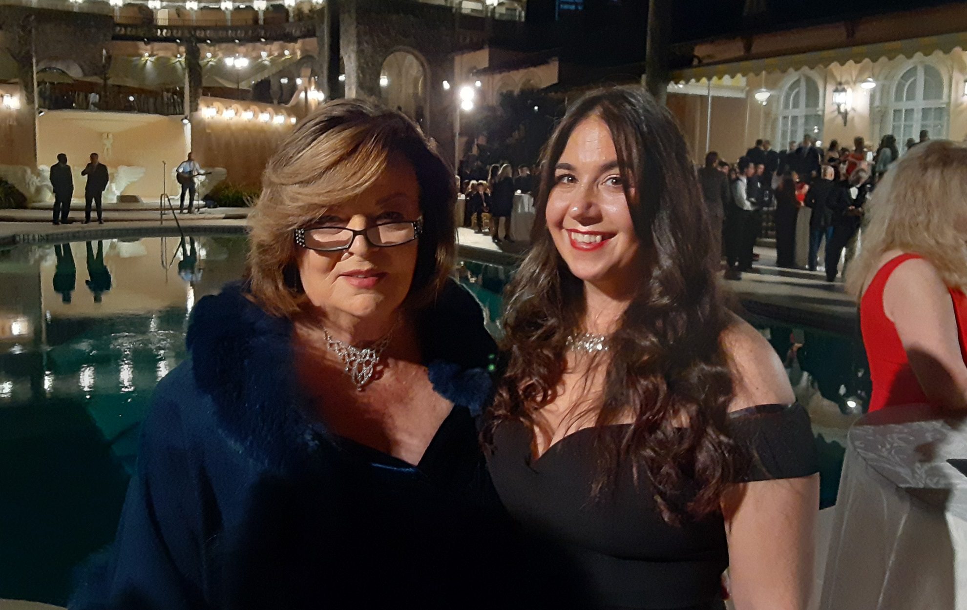 Two women dressed elegantly, smiling at a nighttime event.