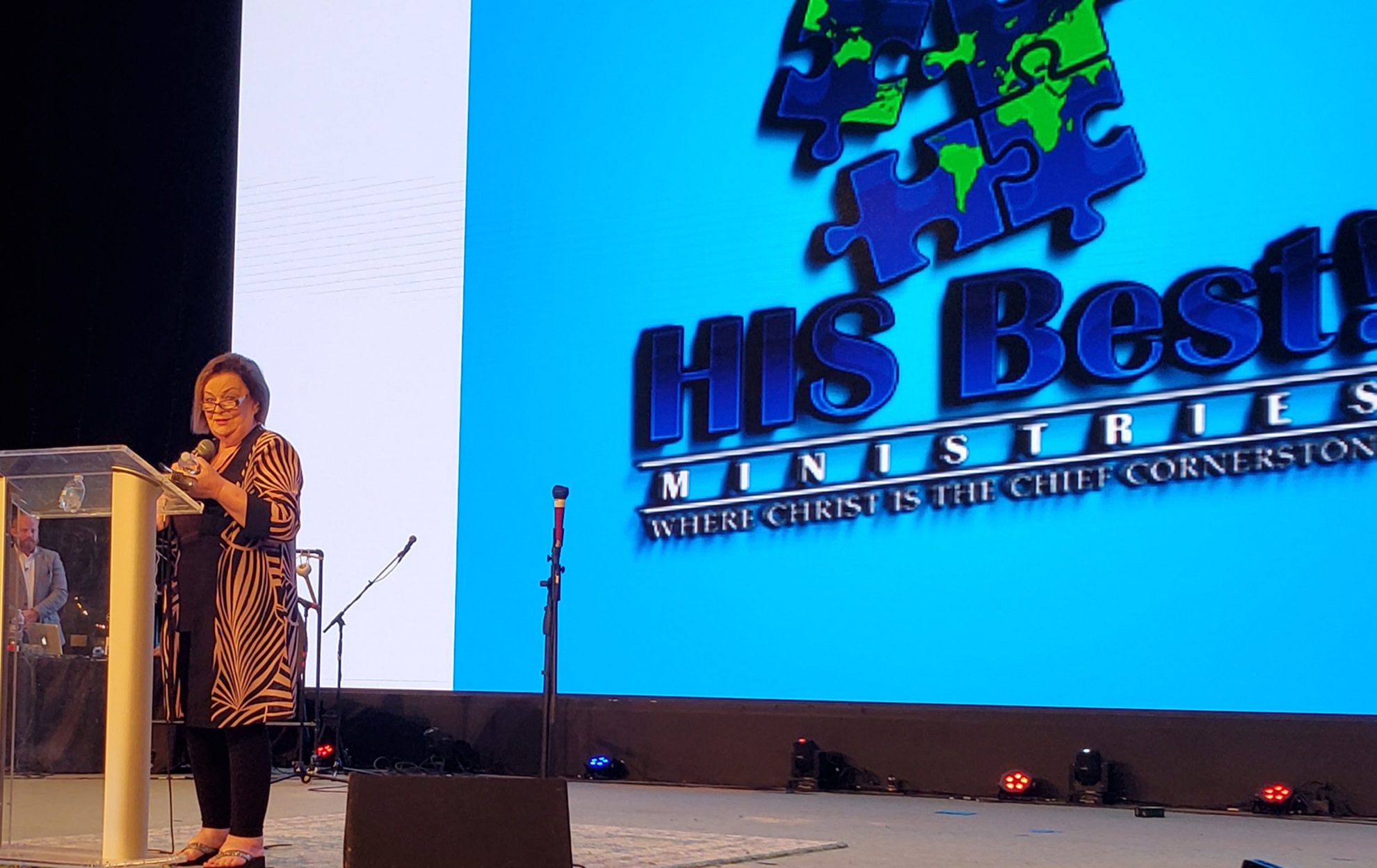 Speaker addressing audience at HIS Media Ministries event with logo on screen.