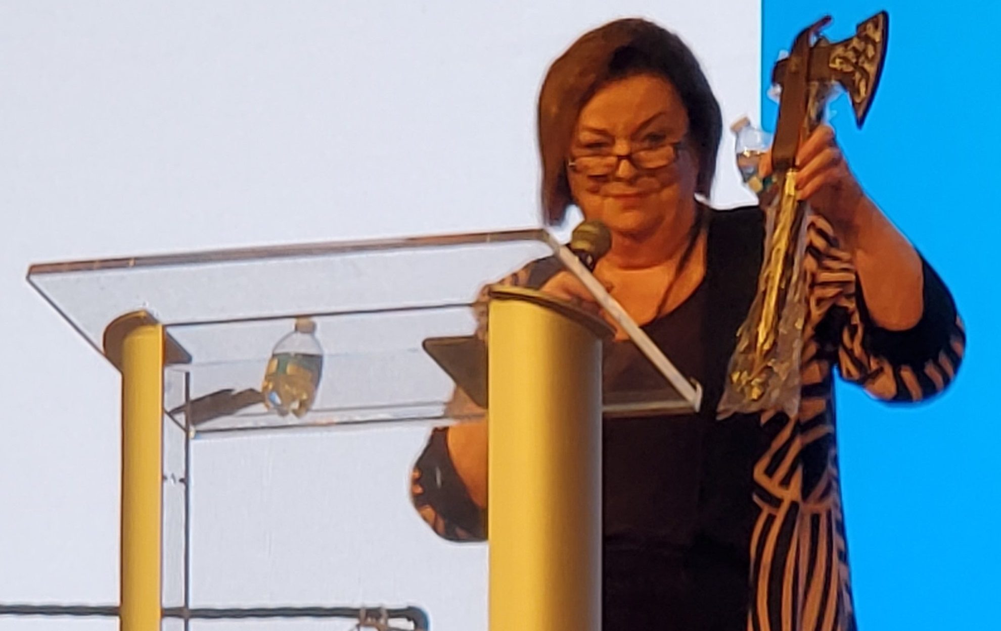 Woman reading at a podium with a microphone and water bottle nearby.