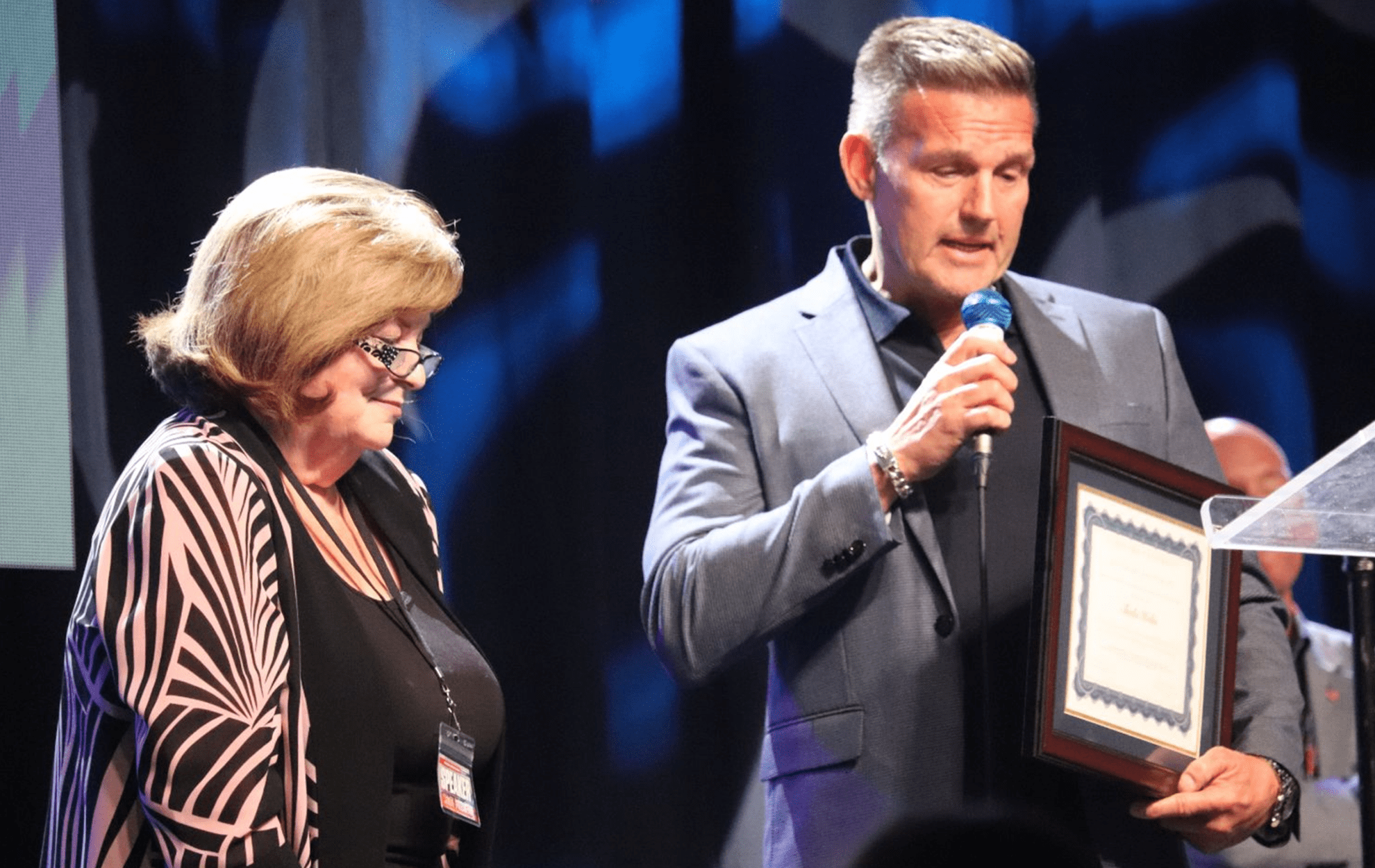 Man receiving an award on stage while a woman looks on.