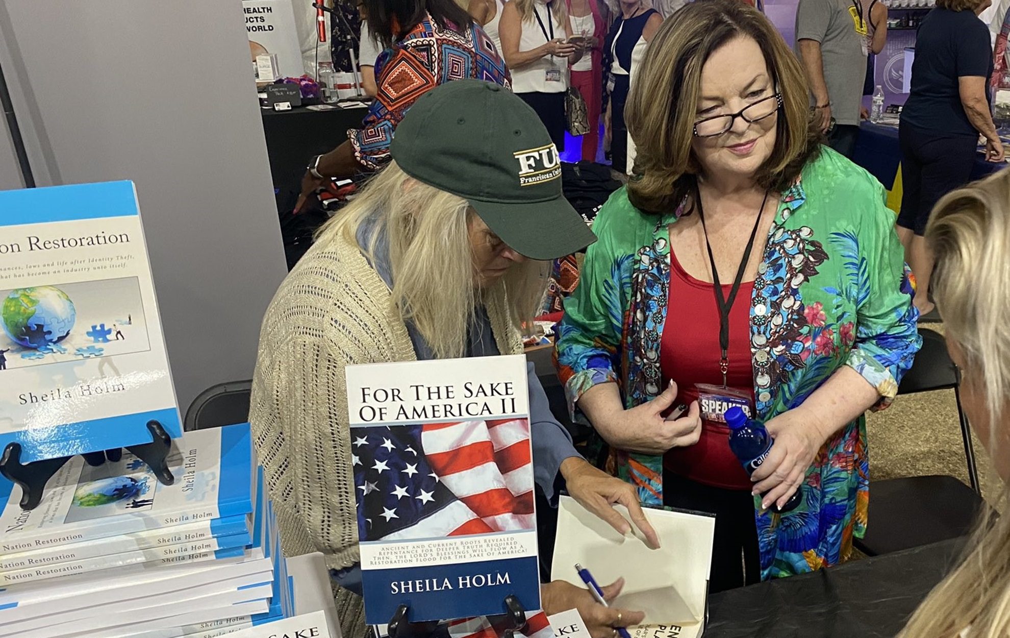 Two women at a booth with chess-themed items and a book.