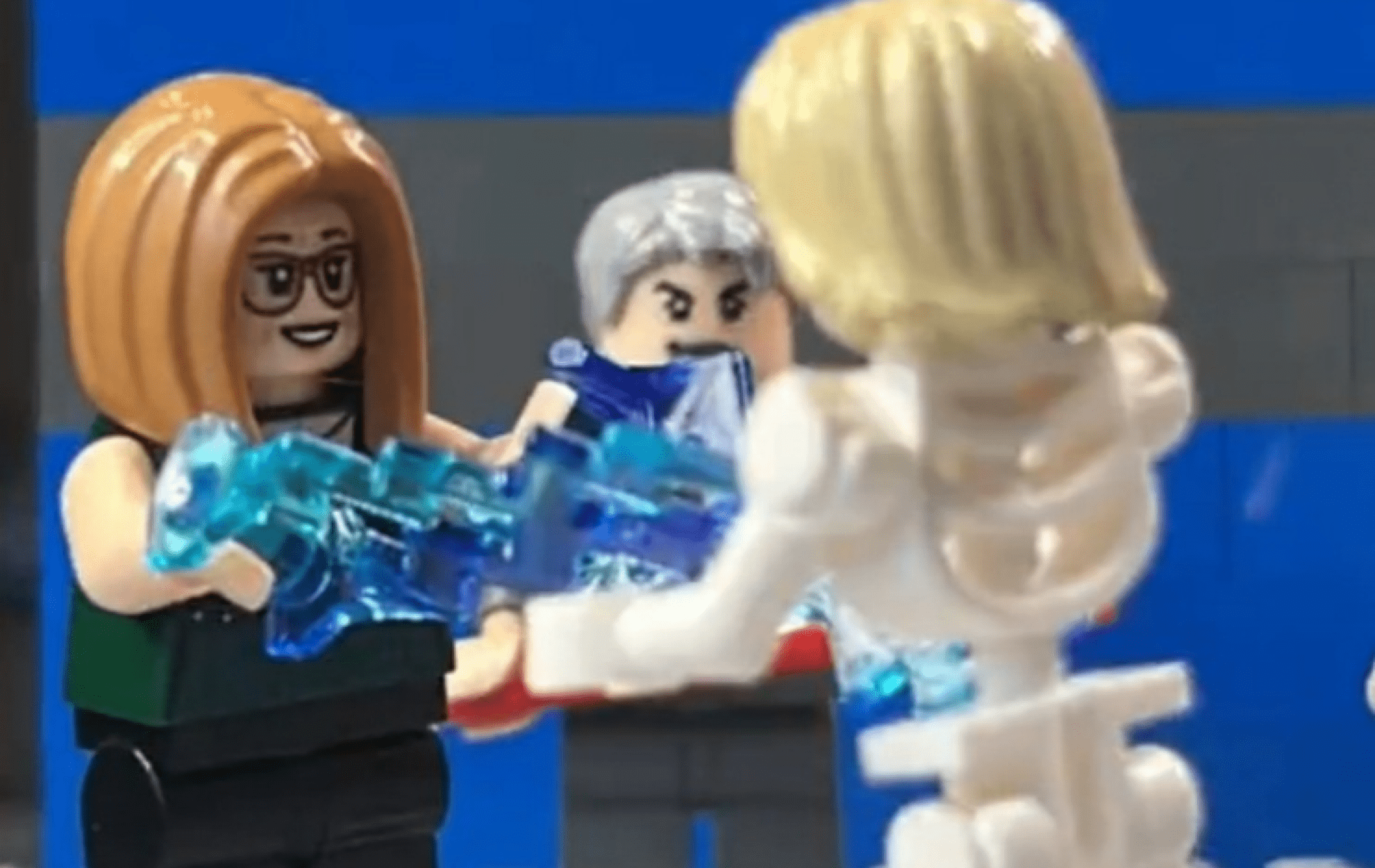 Three LEGO figures interacting, one holding blue translucent pieces.