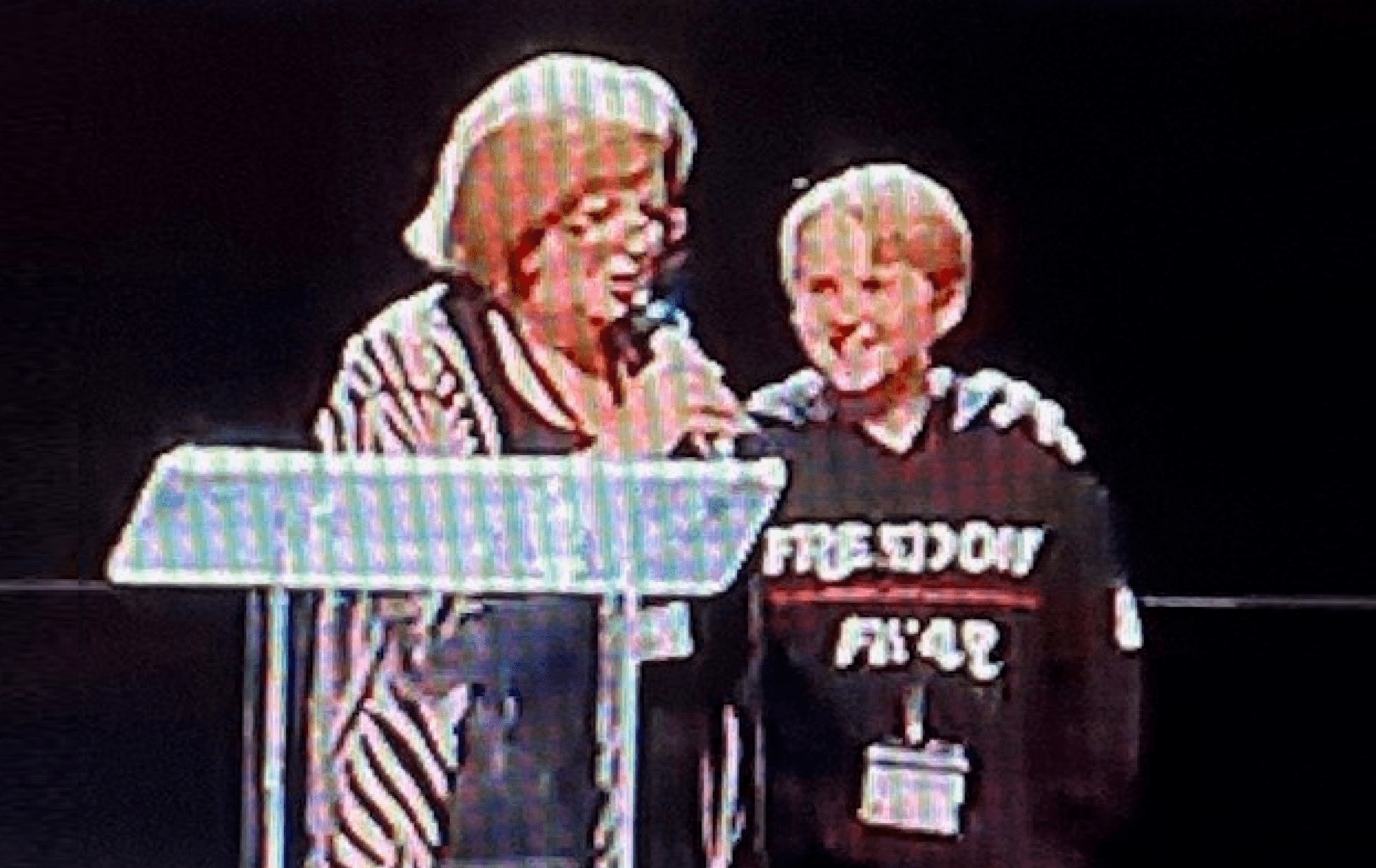 A woman and a boy speak together on stage at a podium.